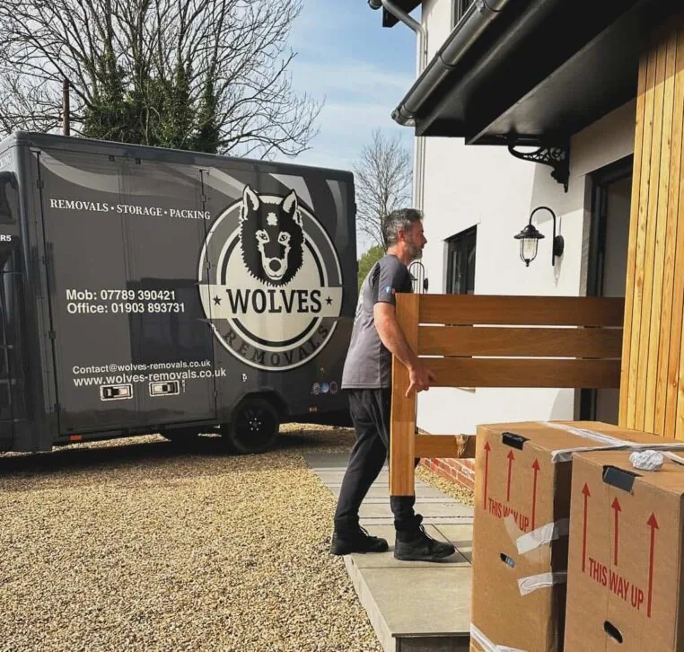 A Wolves Storage Sussex mover carrying furniture past the branded van at a customer&rsquo;s home