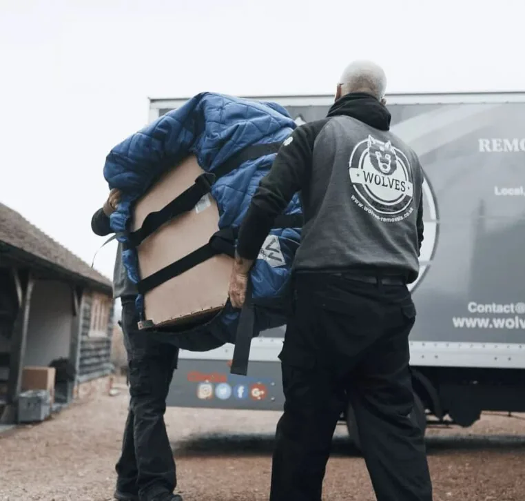 Two Wolves Storage Sussex movers carrying a blanket-wrapped armchair to the van